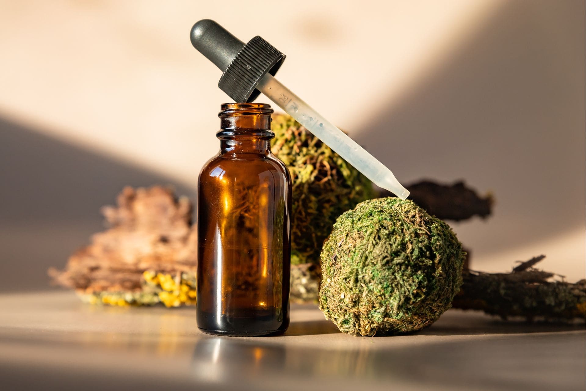 Frasco de vidrio ámbar con pipeta junto a una bola de resina, mostrando formatos de los tipos de CBD disponibles