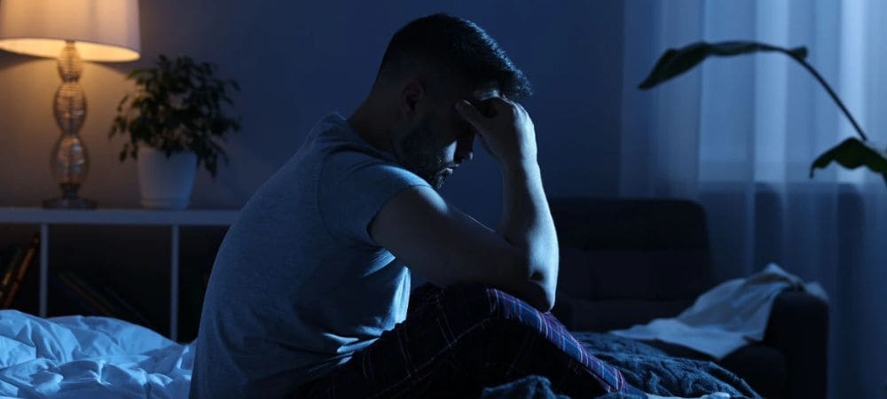 Hombre con insomnio sentado en la cama durante la noche, reflejo de problemas para conciliar el sueño